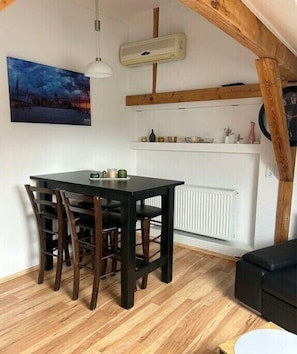 Un comedor con una mesa y sillas de madera, un radiador blanco, un ventilador de techo y un cuadro en la pared.