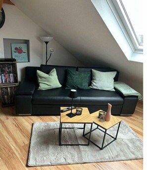 Una sala moderna con un sofá negro, una mesa de centro de madera y un tapete gris.