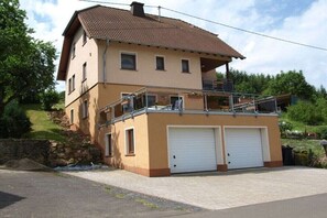 Ein zweistöckiges Haus mit Balkon, zwei Garagen und einer Steinmauer.