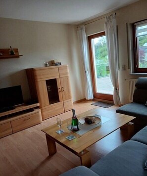 Ein modernes Wohnzimmer mit Fernseher, Holzschrank, Sofa und Esstisch mit Flasche und Gläsern.