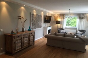A living room with a sofa, wooden cabinet, TV, fireplace, and a window with curtains. - Holiday apartment in Kirchheim with barbecue (Kirchheim)