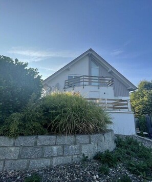 A modern two-story house with a balcony, surrounded by greenery and a stone wall. - Holiday apartment in Kirchheim with barbecue (Kirchheim)