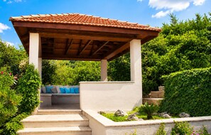 A covered outdoor seating area with steps leading up to it, surrounded by lush greenery. - Beautiful home in Korcula (Korcula)