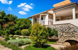 A house with a stone wall, a covered porch, and a garden with various plants. - Beautiful home in Korcula (Korcula)