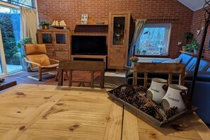 A cozy living room with a brick wall, wooden furniture, a television, and a window with a view of greenery. - Holiday home with 3 bedrooms (Bruinisse)