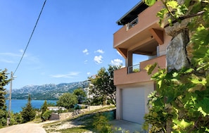 Ein zweistöckiges Gebäude mit Garage, umgeben von viel Grün und einer Berglandschaft.
