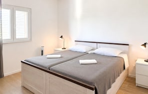 Ein Doppelbett mit Holzvorhang, ein Nachttisch mit Lampe und ein Fenster mit Jalousien.