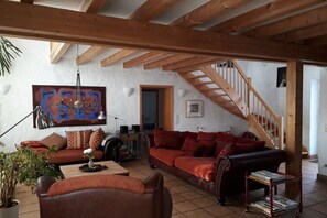 Ein geräumiges Wohnzimmer mit hoher Decke, Holzbalken, einer Treppe und einem großen abstrakten Gemälde.