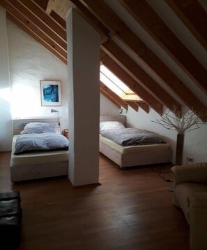 Ein Schlafzimmer im Loft-Stil mit zwei Betten, Holzbalken, einem Oberlicht und einem Bild an der Wand.