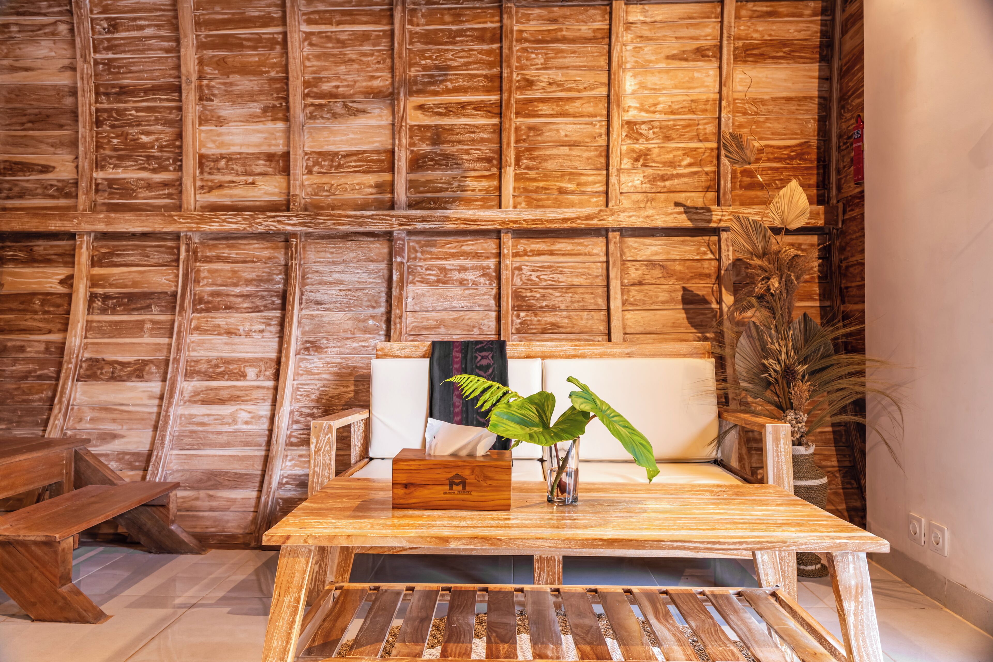 A wooden table with a plant, a bench, and a sofa in a room with wooden panel walls.