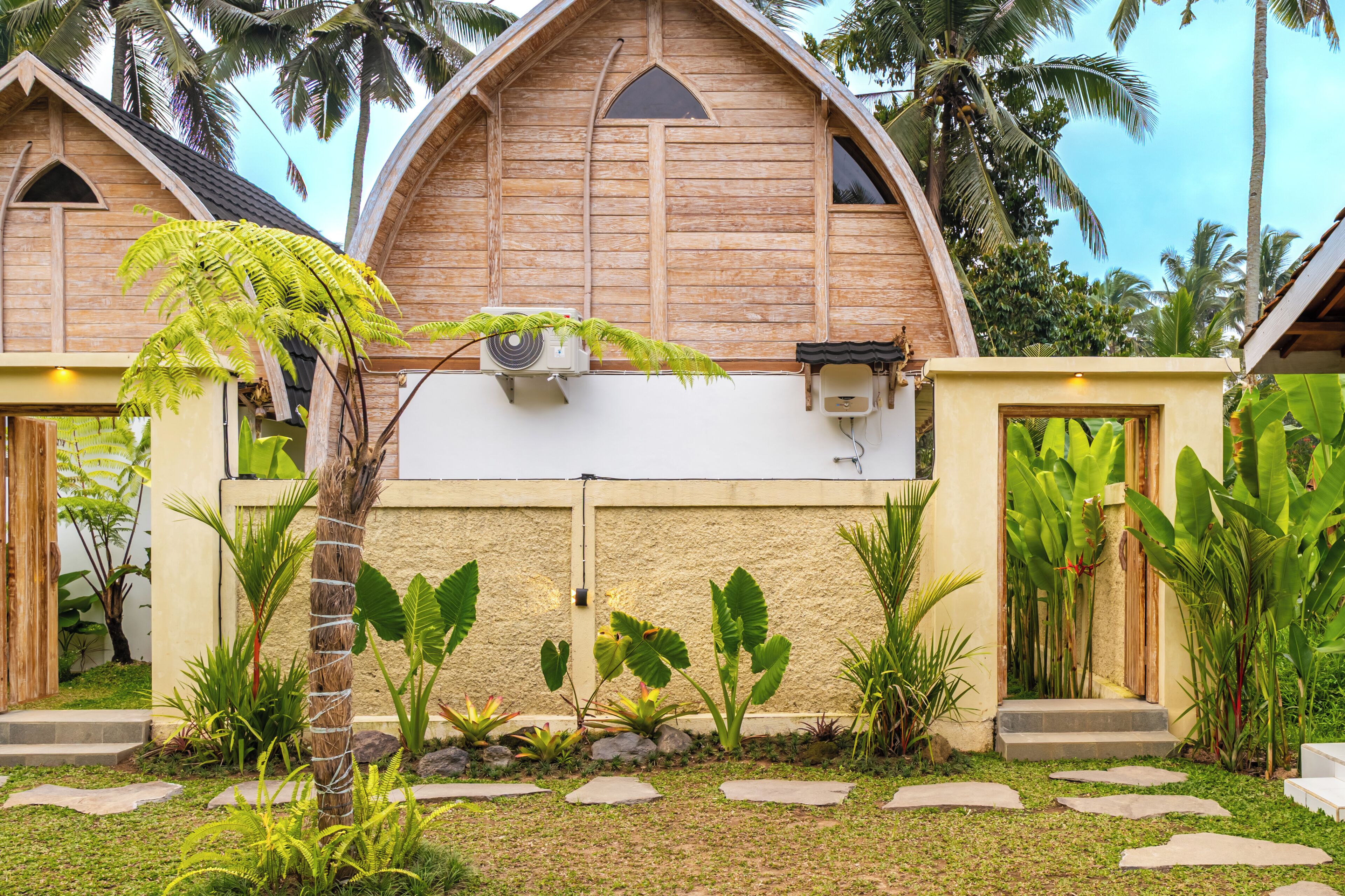 A wooden villa with a sloped roof, surrounded by lush tropical vegetation and a well-maintained garden.