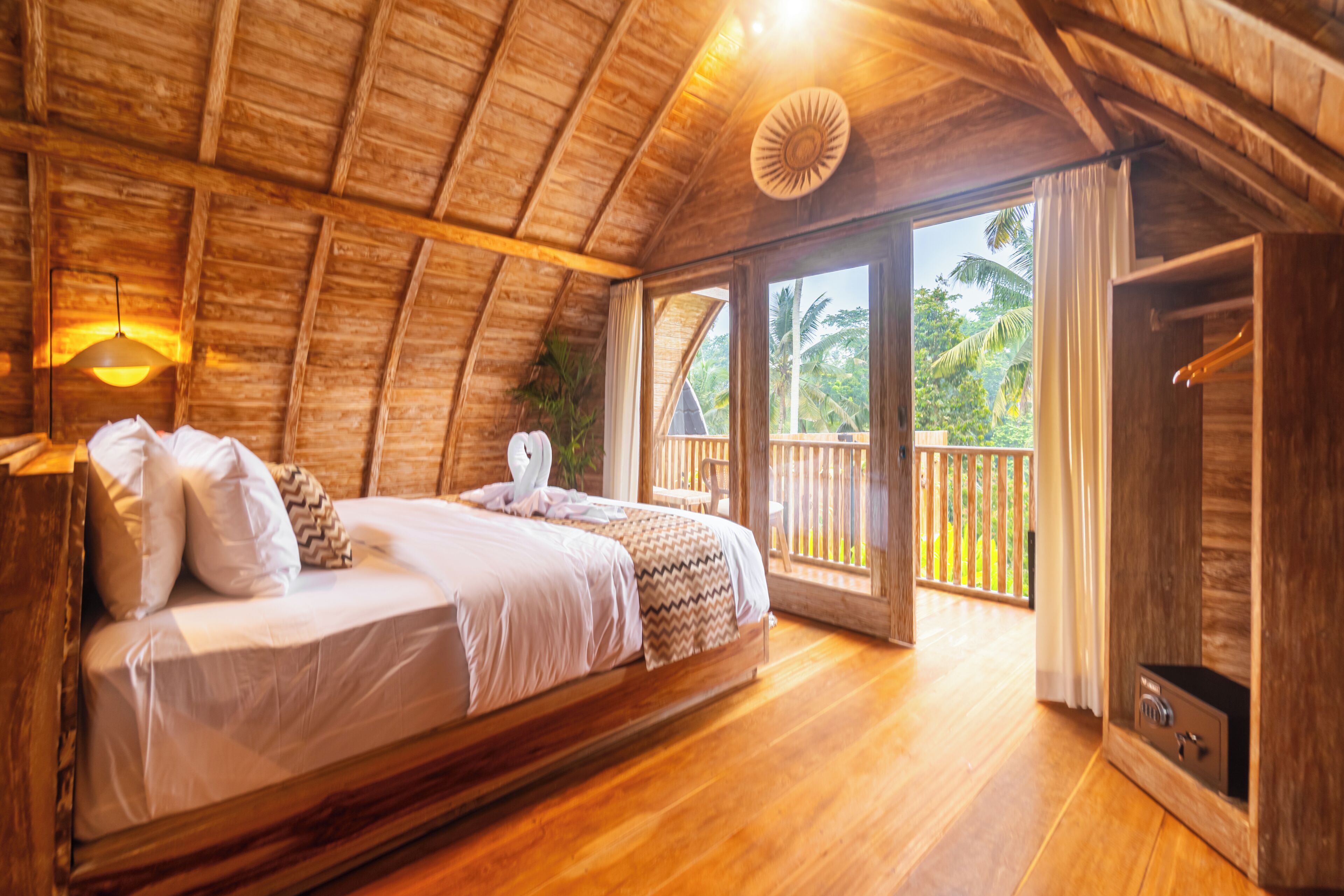 A wooden room with a bed, a nightstand, a lamp, and a view of the outdoors.