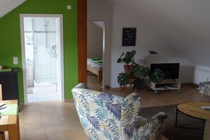 Ein Wohnzimmer mit Sofa, Fernseher, Topfpflanze und einer Tür zum Badezimmer.