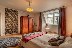 Ein Schlafzimmer mit einem Bett, einem Holzschrank, einem Fenster mit Vorhängen und einer Wand mit Muster.