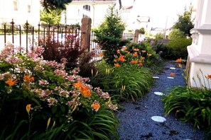 Ein Gartenweg mit verschiedenen Pflanzen und Blumen, eine Steinsitzbank und ein Zaun.