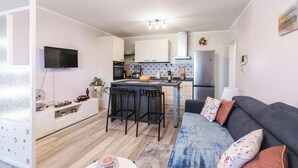 A modern kitchen with a central island, a dining area with bar stools, a flat-screen TV mounted on the wall, and a sofa with floral cushions. - Nice apartment in Krasica with WiFi (Krasica)