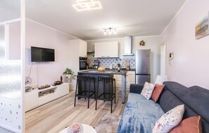 A modern kitchen with a central island, a dining area with bar stools, a flat-screen TV mounted on the wall, and a sofa with floral cushions. - Nice apartment in Krasica with WiFi (Krasica)