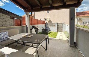 Eine überdachte Terrasse mit Tisch, Stühlen, einem Grill und einem kleinen Rasen.