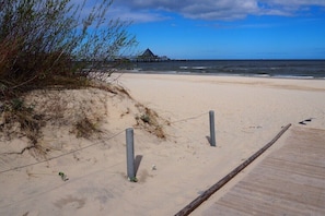 Ein Strand mit einer Holzpromenade, die zu einem Gebäude mit einem dreieckigen Dach führt.