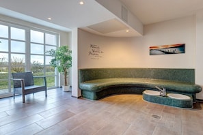 Ein modernes Interieur mit einem gebogenen, grünen Sofa, einer Bank, einer Topfpflanze und einem Wandbild.