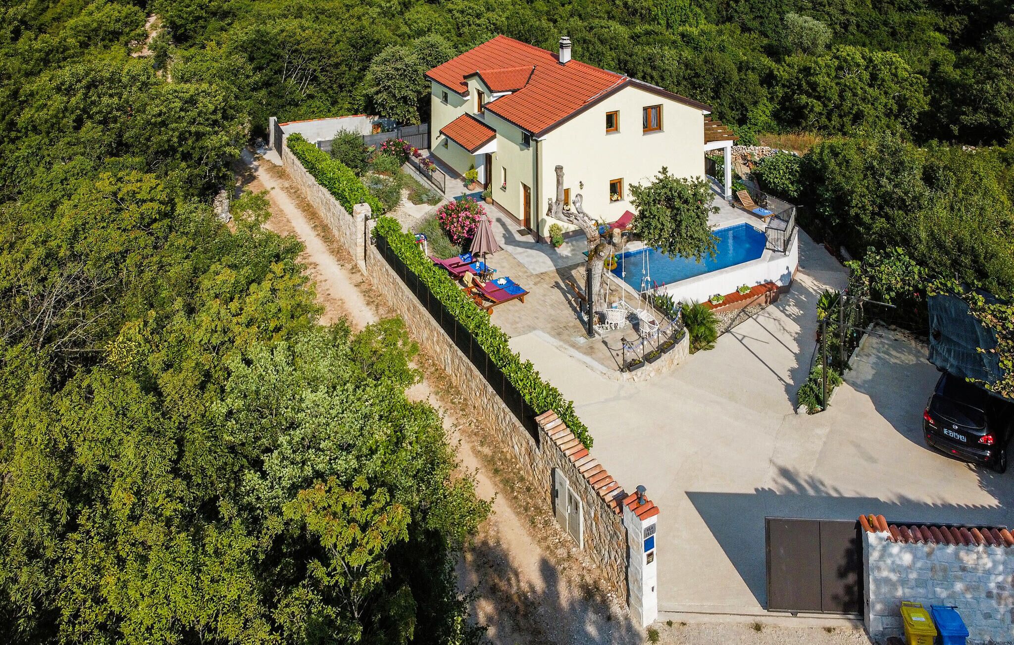 Una casa de dos pisos con piscina, rodeada de vegetación.