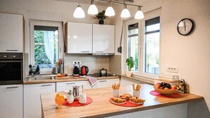 Een moderne keuken met witte kastjes, een houten aanrecht, een waterkoker, een koffiezetapparaat en een klok aan de muur.