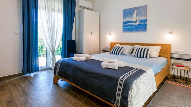 Een slaapkamer met een bed, een schilderij van een zeilboot, een raam met gordijnen en een airconditioner.