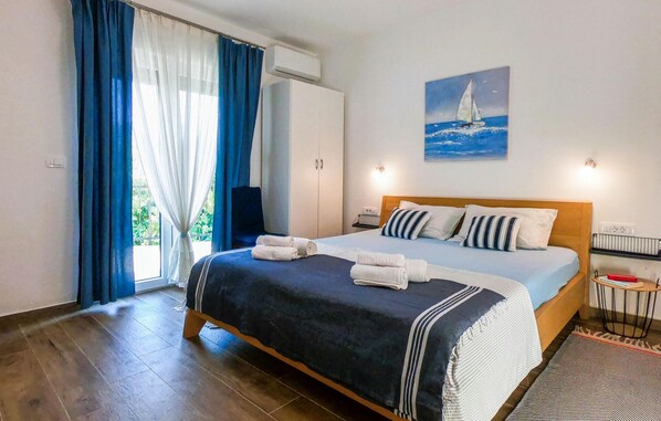 A bedroom with a bed, a painting of a sailboat, a window with curtains, and an air conditioning unit. - Awesome home in Dobrinj (Dobrinj)