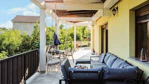 Een overdekt terras met een bank en stoelen, een bijzettafeltje en een hangstoel.