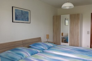 Ein Schlafzimmer mit einem Bett, einem Nachttisch, einer Lampe, einem Kleiderschrank und einem gerahmten Bild an der Wand.