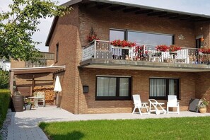 Ein zweistöckiges Haus mit Balkon, Außenbereich zum Sitzen und einer überdachten Terrasse.