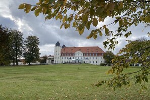 Ein großes Gebäude mit rotem Dach und zwei Kuppeln, umgeben von einer grünen Wiese und Bäumen.