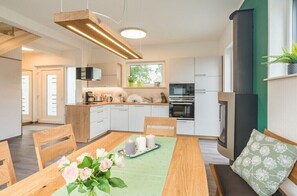 Eine moderne Küche mit weißen Schränken, einem eingebauten Ofen sowie einem Essbereich mit einem Holztisch und Stühlen.