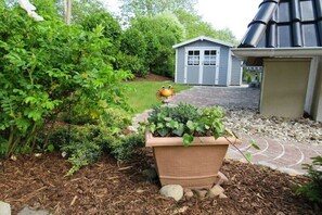 Ein Garten mit einem Blumenkasten, einem Gartenhaus und einem Haus mit gewundener Dachform.