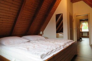 Ein Schlafzimmer mit schrägen Wänden, einem Bett mit weißer Bettwäsche und einer Tür zu einem anderen Raum.