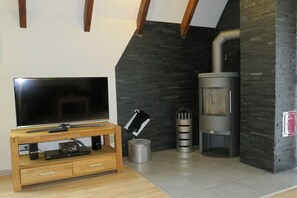 Ein Wohnzimmer mit Flachbildfernseher auf Holzständer, Steinwand und Kaminofen.