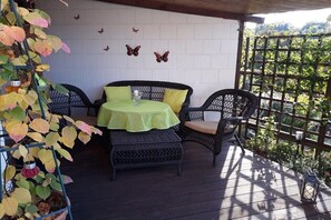 Eine überdachte Terrasse mit Korbmöbeln, einem Tisch mit grüner Tischdecke und einer Wand mit Schmetterlingsdekorationen.