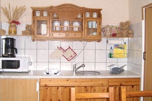 Una cocina con microondas, cafetera, armarios de madera y un lavamanos.
