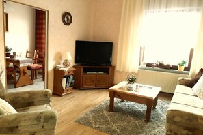 Ein Wohnzimmer mit Fernseher, Sofa, Couchtisch und einem Essbereich mit Tisch und Stühlen.