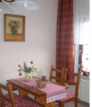 Ein Esstisch mit kariertem Tischtuch, einer Blumenvase, einem Teddybären und einem Stuhl.