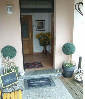 Un felpudo, un cartel, una puerta, un jarrón con girasoles y dos plantas en macetas.