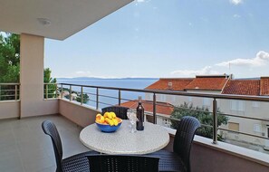 Ein Balkon mit Tisch, Stühlen, einer Obstschale und einer Flasche.