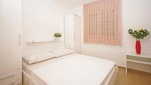 Una camera da letto con un letto, un armadio, uno scaffale con una pianta e una finestra con tende.