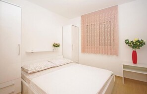 A bedroom with a bed, a wardrobe, a shelf with a plant, and a window with curtains. - Awesome apartment in Brela with swimming pool (Brela)