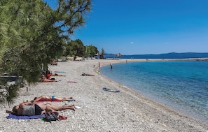 A pebble beach with people sunbathing and swimming, a pier in the background, and clear skies. - Awesome apartment in Brela with swimming pool (Brela)