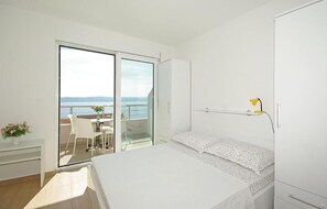 Ein Schlafzimmer mit Bett, Schreibtisch, Stuhl, einem kleinen Tisch mit Blumen, einem Balkon mit Blick und einem Nachttisch.