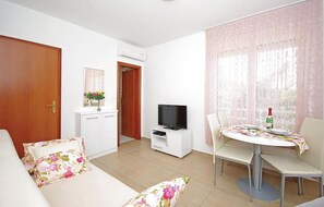 Ein Wohnzimmer mit einer Couch, einem Fernseher, einem Esstisch und Stühlen.