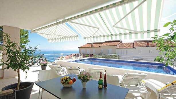 A poolside area with a table, chairs, and a view of the sea. - Lovely apartment in Brela with WiFi (Brela)