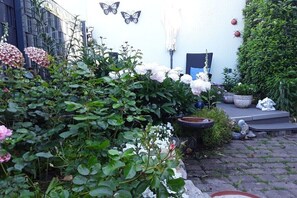 Um jardim com diversas plantas e flores, uma porta azul e uma parede branca com detalhes de borboletas.