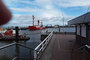 Um porto com um navio vermelho atracado, um cais e um edifício com uma persiana fechada.